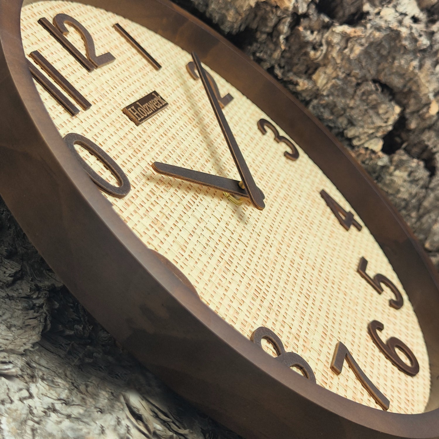 Schrägaufnahme der Holzwerk PENZBERG Funk-Wanduhr aus Vollholz mit Rattan-Design und brauner Zeigerführung